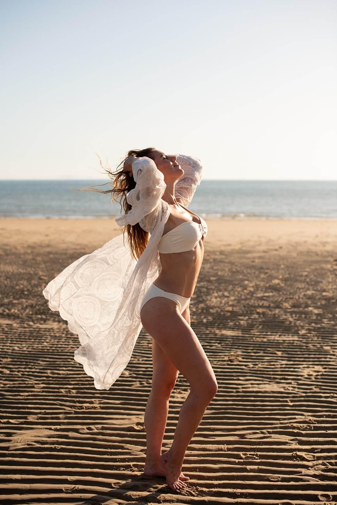 Portret van de zijkant van een lachende vrouw in witte bikini en kanten kimono genietend van de zon op het strand