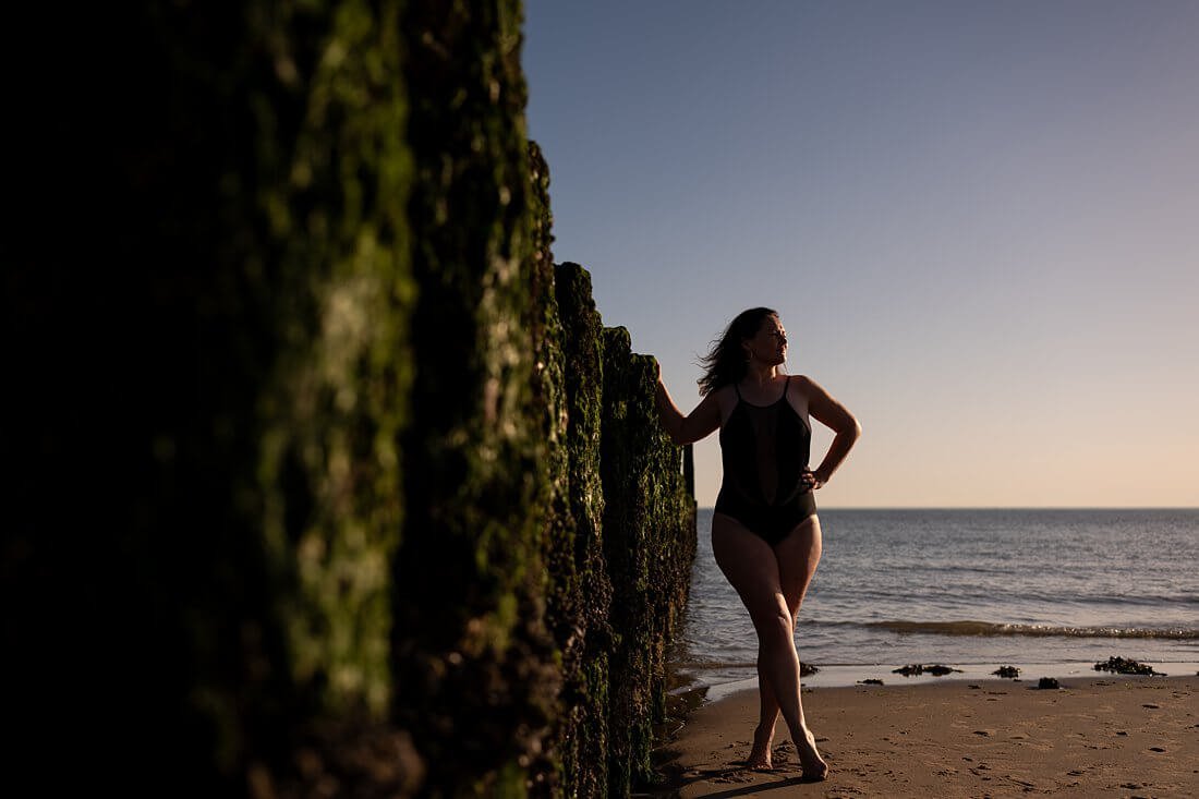 Onderbelichte foto van een vrouw in zwart badpak bij de houten strandpalen van Dishoek met een spannend spel van schaduwen.