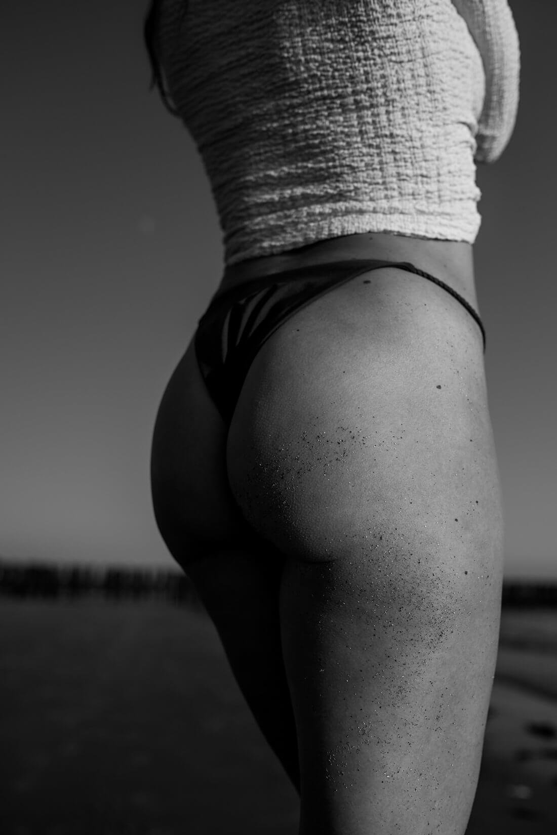 Zwart-wit close-up van de billen van een vrouw in bikini met plakkend zand op het strand