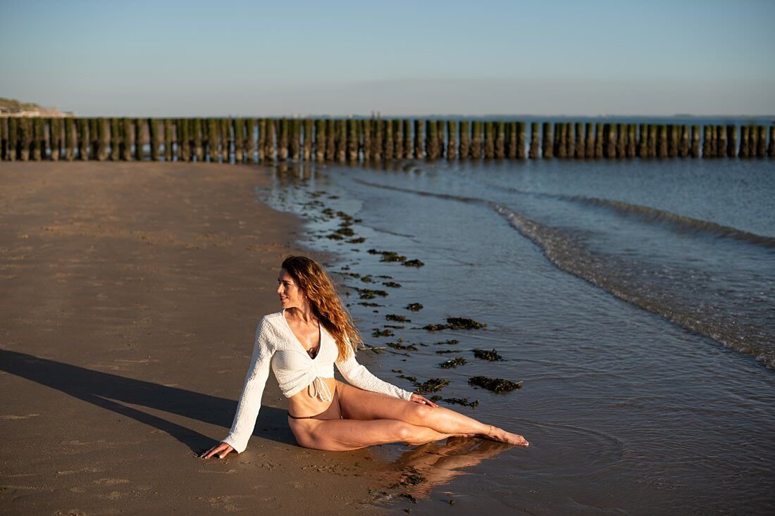Vrouw in zeemeermin pose in de branding van Dishoek met de iconische houten strandpalen op de achtergrond