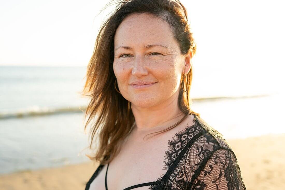 Zelfverzekerd portret in kleur van een vrouw die in de camera kijkt, omringd door het gouden uur tegenlicht tijdens een boudoir strand shoot.