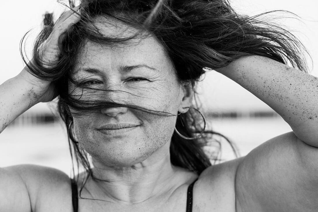 Krachtig zwart-wit portret van een vrouw met beide handen in haar haren die sterk in de camera kijkt tijdens een boudoir fotoshoot.