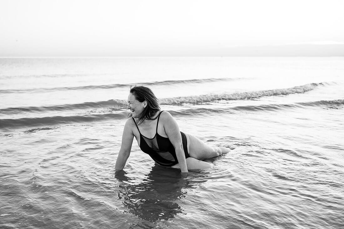 Hard lachende vrouw in zeemeermin pose in het water van de zee tijdens een fotosessie in zwart-wit.