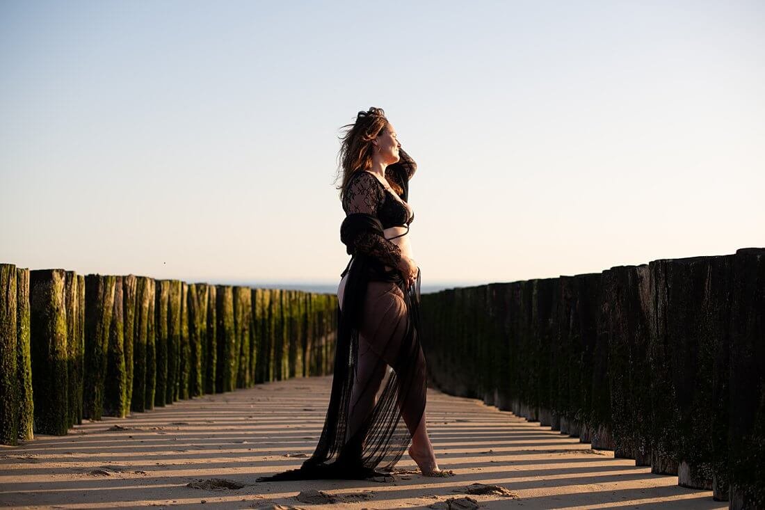 Close beeld in kleur van een sierlijke vrouw met haar hand in haar haren die boven de strandpalen in Dishoek uitsteekt met prachtig licht op haar curves.