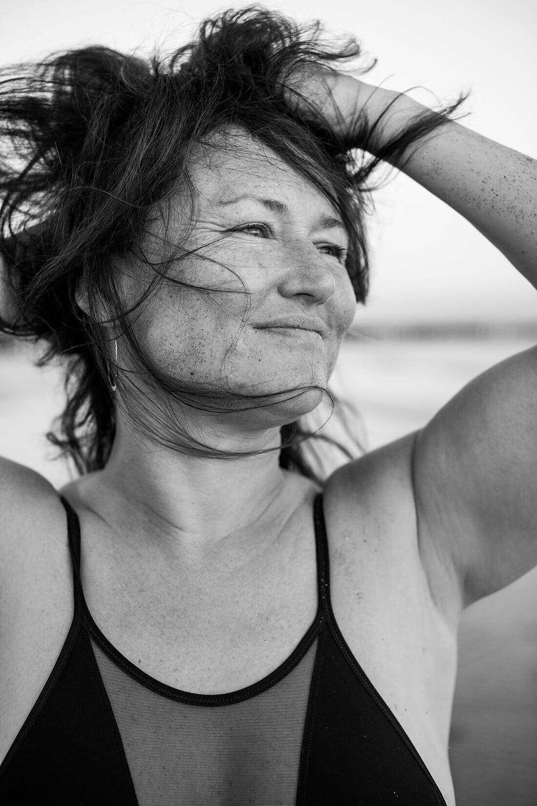 Zwart-wit portret van een zelfverzekerde vrouw die met haar handen door haar wilde haren speelt op het strand.