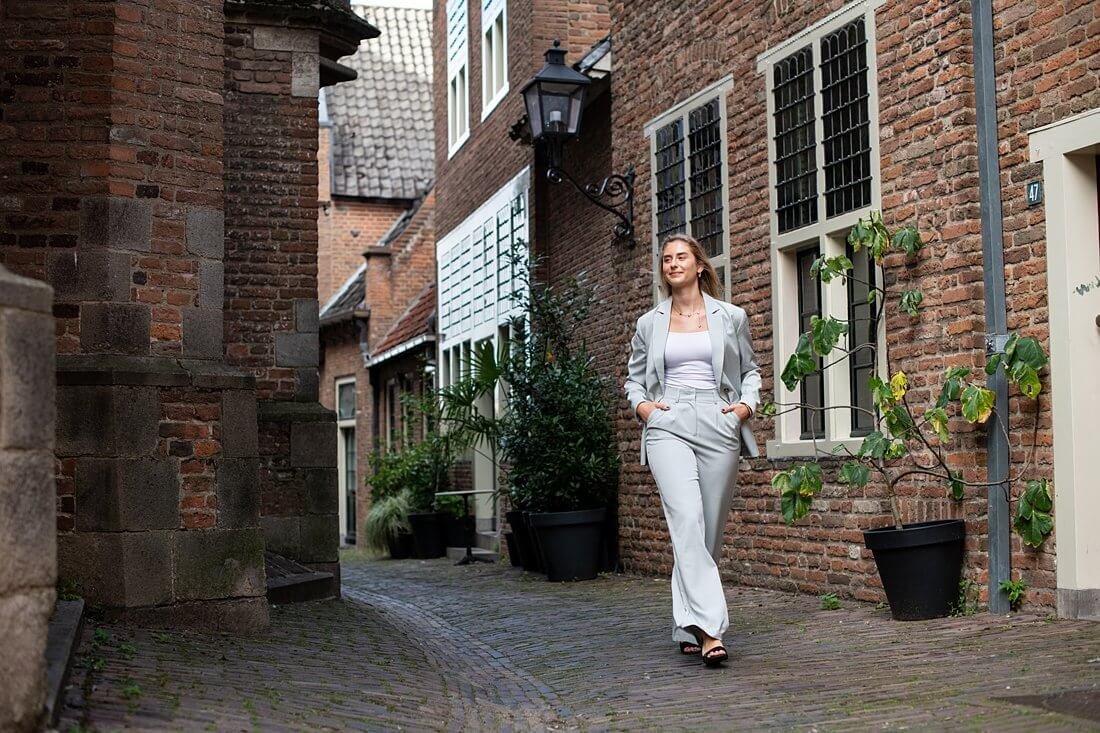 Vrouwelijke ondernemer wandelend in lichtgrijs pak door de straten van Nijmegen.