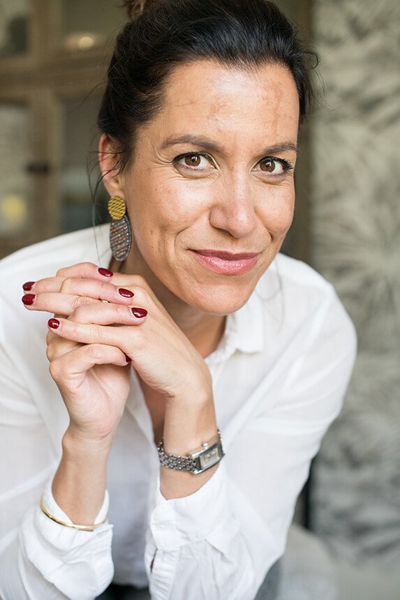 Vrouw met zelfverzekerde glimlach kijkt recht in de camera, draagt een witte blouse – portretfotografie in Breda/Brabant.