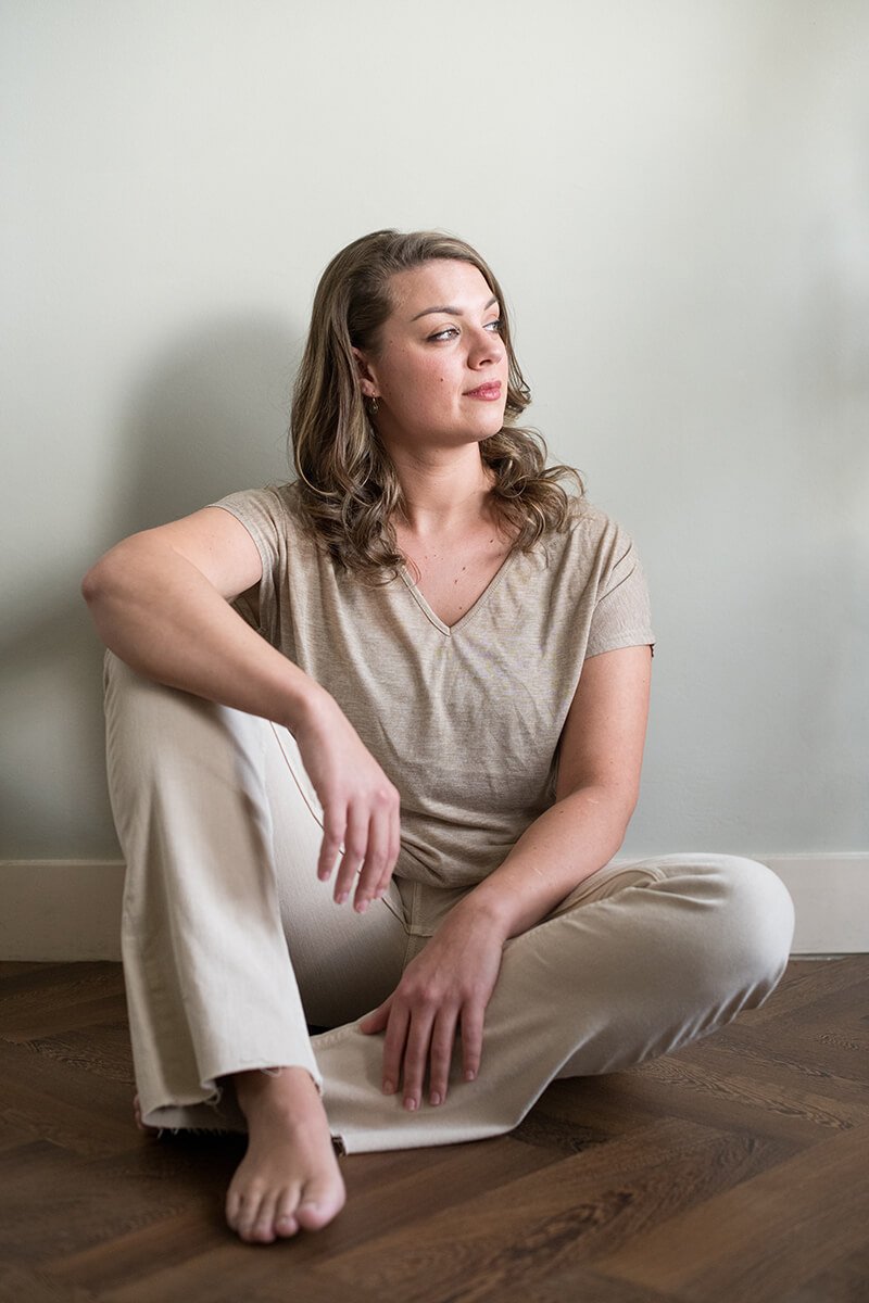 Persoonlijke fotografie met aandacht en rust – Breda Vrouw zittend tegen een muur met een rustige en open blik, gefotografeerd door een fotograaf in Breda