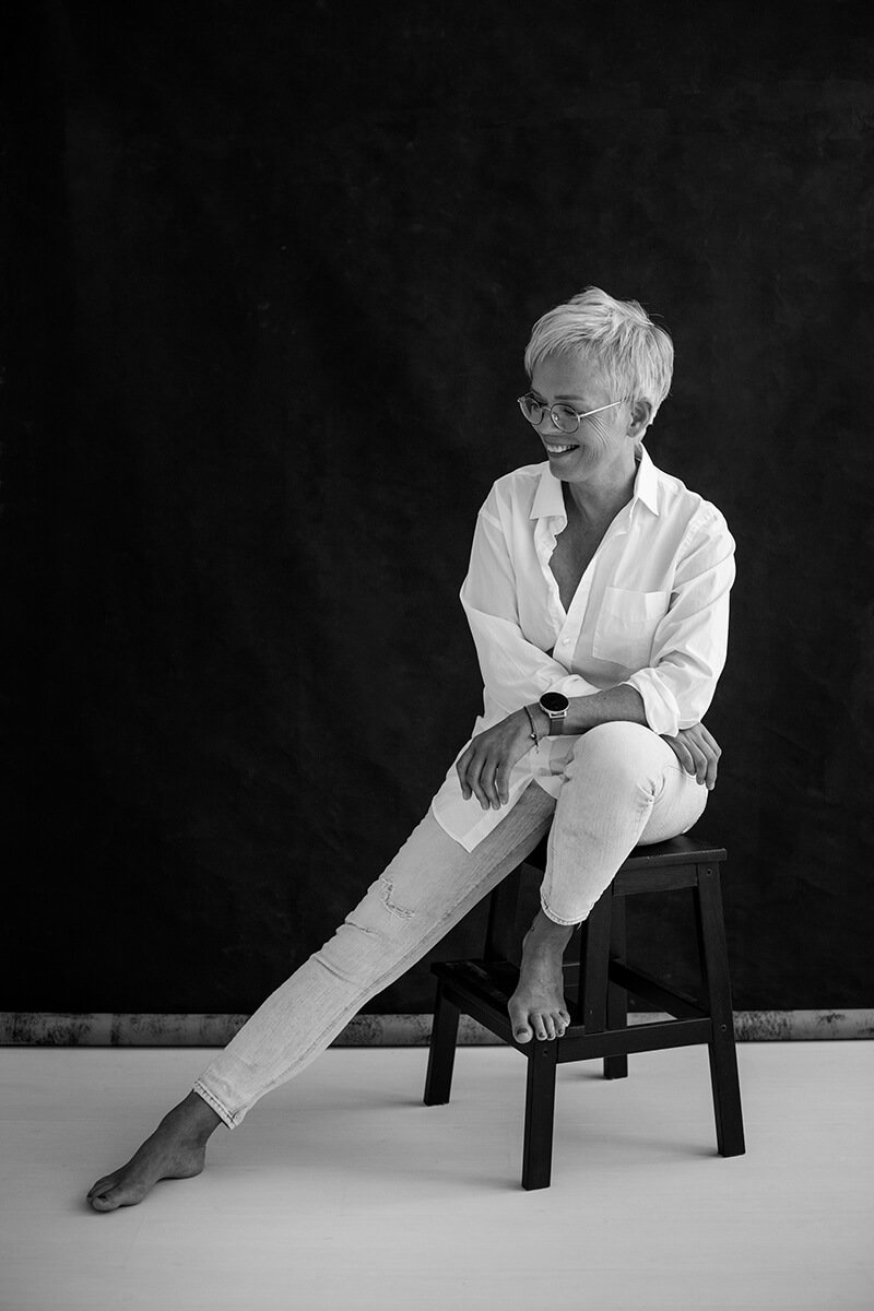 Portret van oudere vrouw zittend op kruk met gestrekt been, ontspannen en krachtig gefotografeerd in Breda