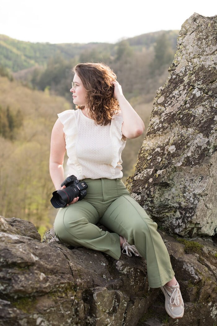 Zelfverzekerde fotografe poseert met camera en hand in haar haar, personal branding in de Ardennen.