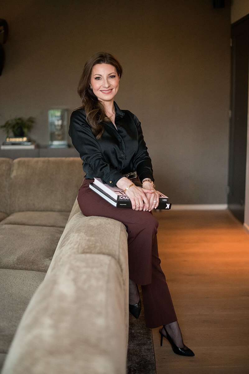 High-end personal branding fotografie in Breda van een fashion-ondernemer met boeken op een bank, zelfverzekerde blik.