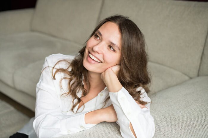 Ontspannen lachende ondernemer zittend op de grond tegen een bank tijdens haar personal branding fotoshoot in Breda.