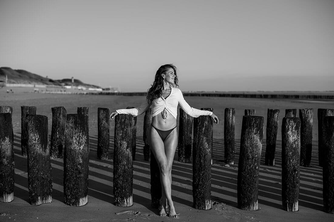 Zwart-wit foto van een lachende vrouw genietend met ogen dicht poserend voor de strandpalen van Dishoek